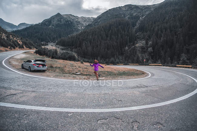 Mujer joven saltando en la carretera de montaña, Draja, Vaslui, Rumania - foto de stock