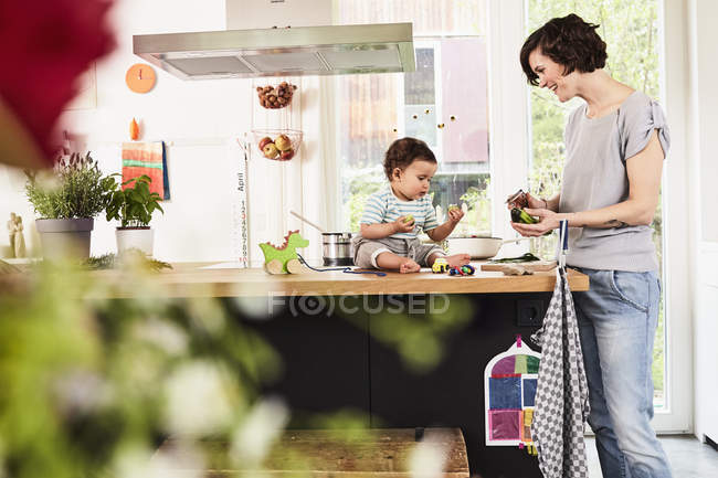 Baby daughter sitting on kitchen counter while mother cooking — Stock Photo