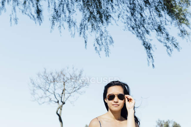 Porträt einer jungen Frau im Freien, die eine Sonnenbrille aufsetzt — Stockfoto