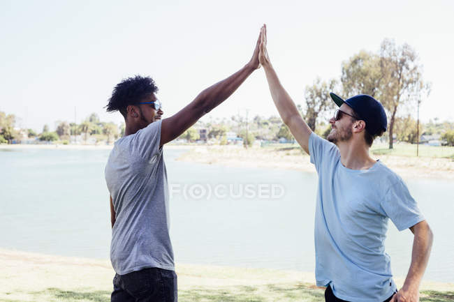 Amis faisant haute cinq près du lac, Long Beach, Californie, États-Unis — Photo de stock
