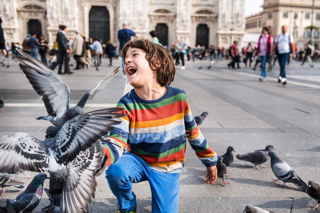 Мальчик смеется, кормя голубей на площади, Милан, Ломбардия, Италия — стоковое фото