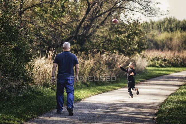 Padre e hijo jugando con la pelota en el camino - foto de stock