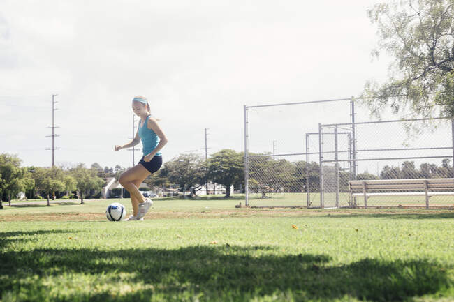 Studentessa facendo dribbling calcio palla pratica sul campo sportivo della scuola — Foto stock