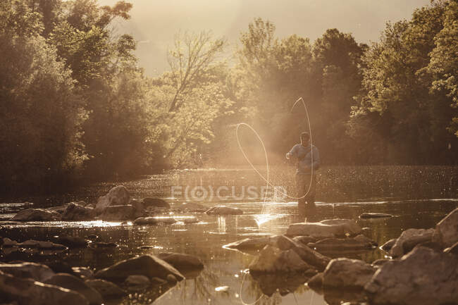 Рыбак, закручивающий леску в залитой солнцем реке, Мозирье, Брезовица, Словения — стоковое фото