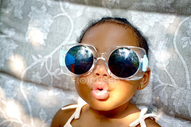 Baby girl sitting on lounge chair wearing sunglasses, portrait — Stock Photo