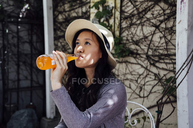 Junge Frau sitzt draußen und trinkt aus Flasche — Stockfoto