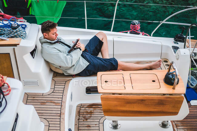 Мужчина отдыхает на борту яхты, смотрит на цифровой планшет, Хорватия — стоковое фото