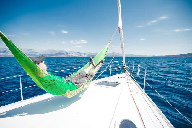 Hombre reclinado en hamaca a bordo de un yate cerca de la costa, Croacia - foto de stock