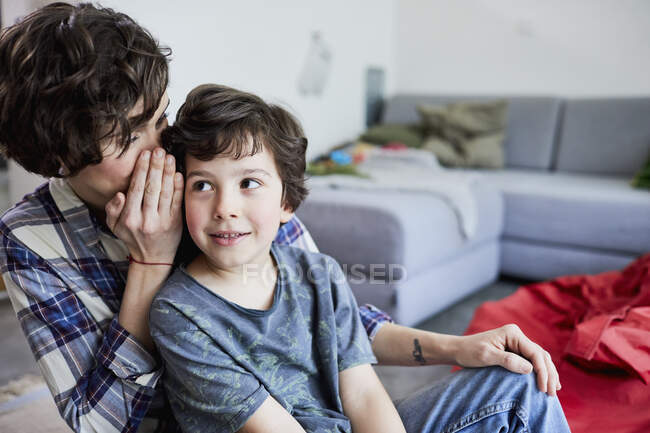 Mother and son at home, mother whispering into son's ear — Stock Photo