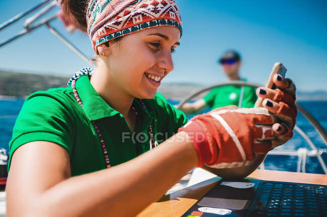 Молодая женщина смотрит на смартфон на борту яхты возле побережья, Хорватия — стоковое фото