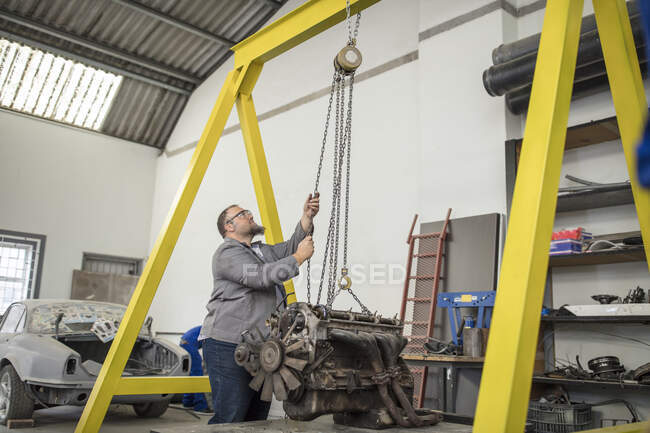Male car mechanic hoisting car engine in repair garage — Stock Photo