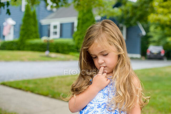 Chica con el dedo en la boca en la acera suburbana - foto de stock
