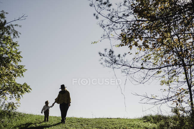 Madre e hija caminando de la mano en un entorno rural - foto de stock