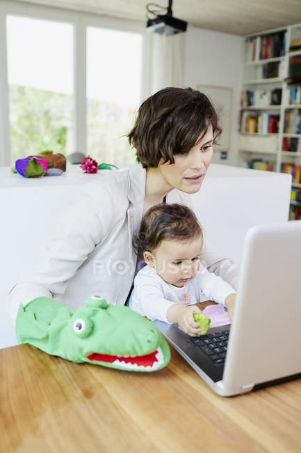 Мать держит девочку на коленях и использует ноутбук — стоковое фото