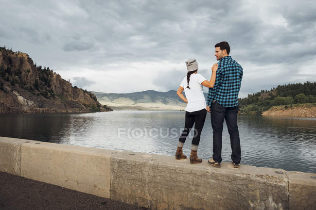 Couple standing on wall beside Dillon Reservoir, looking at view, rear view, Silverthorne, Colorado, USA — Stock Photo