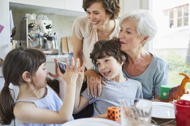 Young girl photographing, brother, mother and grandmother, using smartphone — Stock Photo
