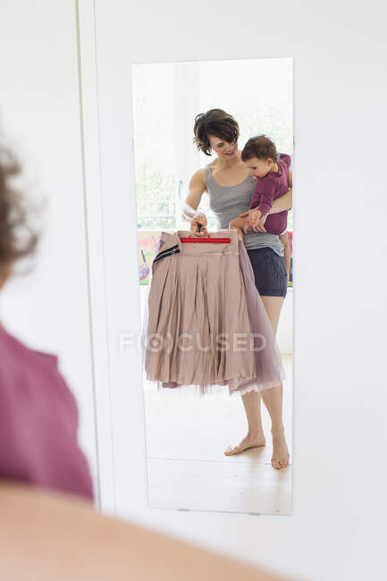 Mother holding baby daughter, holding different outfits in hand — Stock Photo