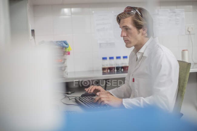 Worker in thread factory, sitting at desk, using computer — Stock Photo