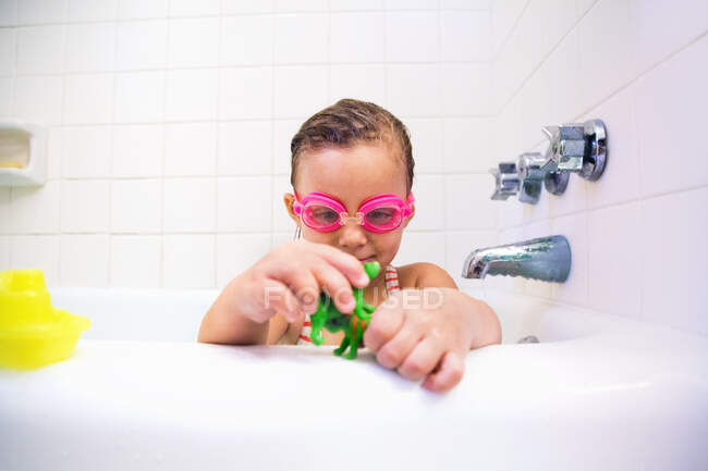 Girl wearing swimming goggles playing with toys in bath — Stock Photo