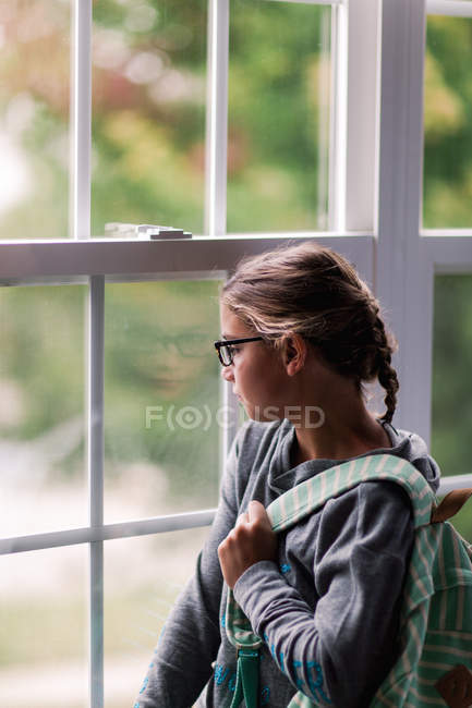 Menina com mochila olhando através da janela da casa — Fotografia de Stock