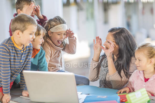 Серед дорослої жінки, яка сиділа з малими дітьми, дивлячись на ноутбук. — стокове фото