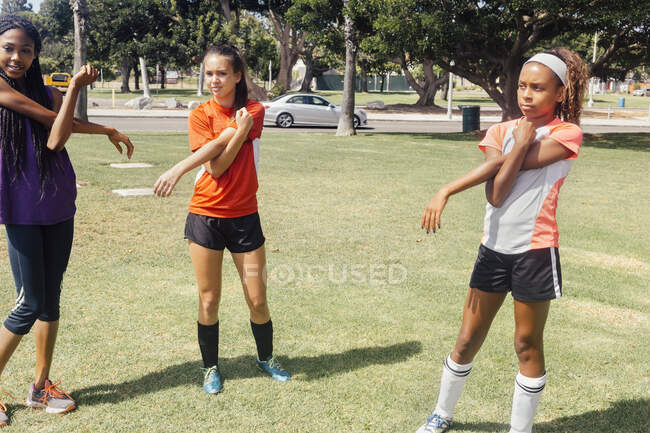 Schoolgirl soccer players stretching arms warming up on school sports field — Stock Photo