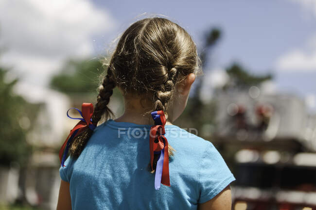Menina com cabelos entrançados, fitas vermelhas e azuis no cabelo, visão traseira — Fotografia de Stock