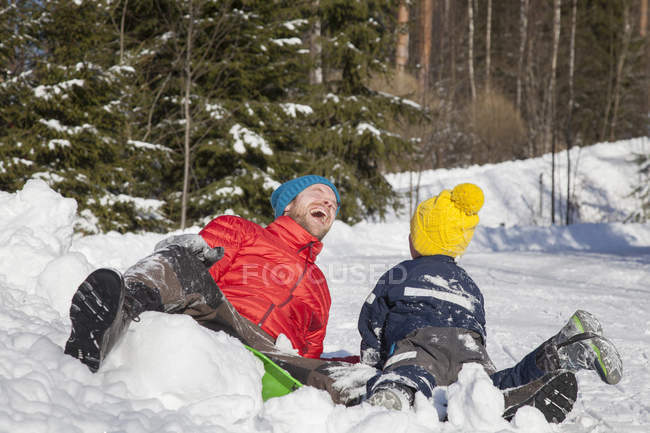 Мужчина и сын смеются после падения в снег — стоковое фото