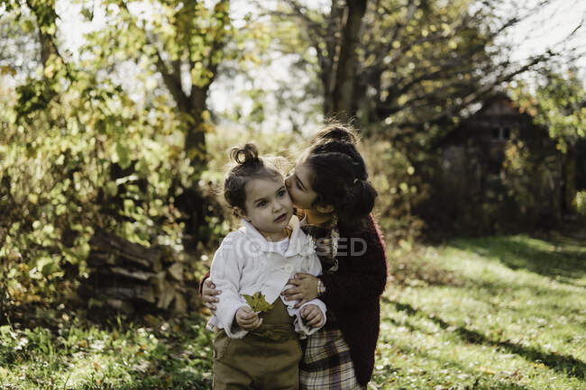 Chica abrazando a hermana menor, en un entorno rural - foto de stock