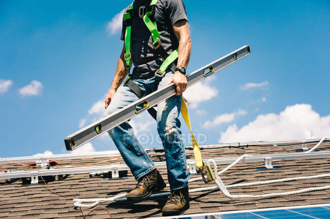 Workman instalando paneles solares en el techo de la casa, manteniendo el nivel de espíritu, sección baja, vista de ángulo bajo - foto de stock