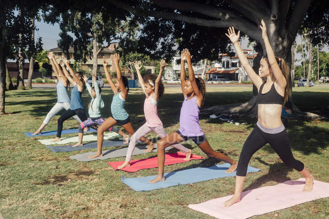 Alunas praticando ioga guerreiro uma pose no campo de esportes da escola — Fotografia de Stock