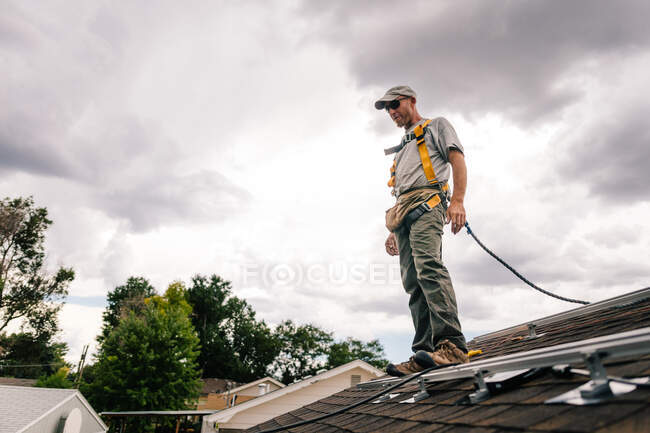 Рабочий на крыше дома, готовится к установке солнечных панелей, вид под низким углом — стоковое фото