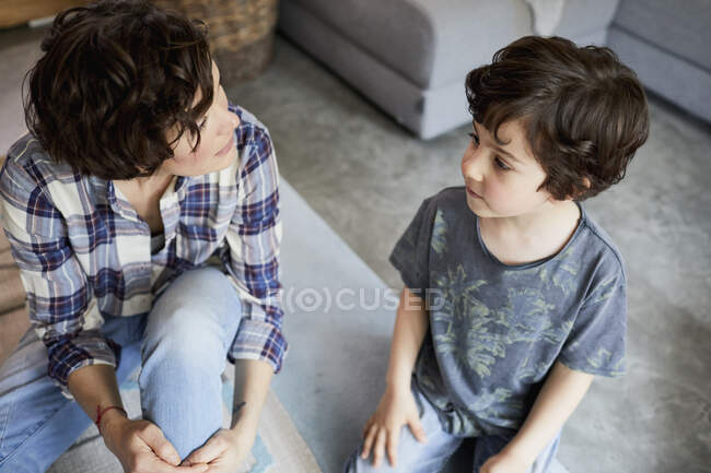 Madre e hijo en casa, sentados en el suelo, hablando - foto de stock