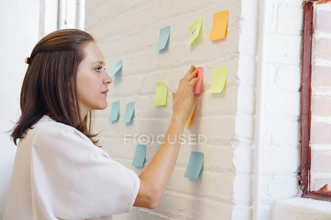 Mujer pegando notas adhesivas a la pared de ladrillo - foto de stock