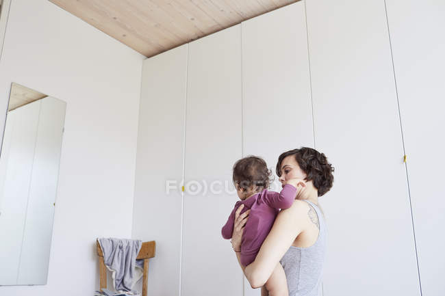 Mother holding baby girl against mirror in bedroom — Stock Photo