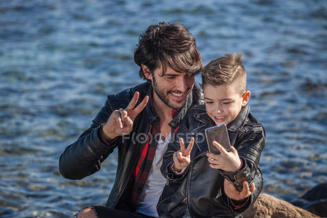 Pai e filho ao lado do mar tomando selfie — Fotografia de Stock