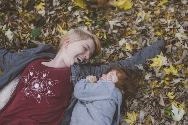 Rothaarige Kleinkind und junge Frau legen sich auf Herbstblätter — Stockfoto