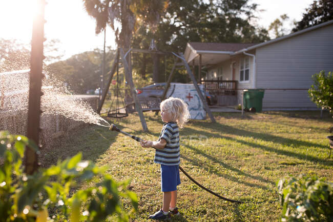 Мальчик распыляет воду из шланга — стоковое фото