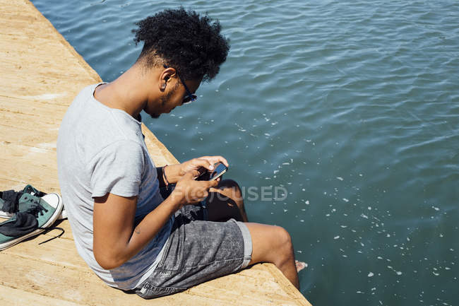 Homem usando telefone celular pela borda da água — Fotografia de Stock