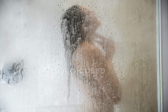 Young woman in shower behind steamed glass door — Stock Photo
