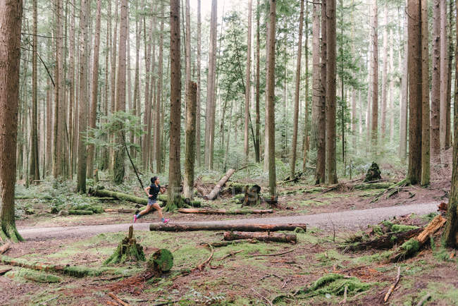 Vista lateral de la mujer corriendo en el bosque, Vancouver, Canadá - foto de stock