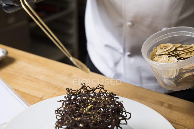 Chef posizionare fette di banana secca sulla decorazione torta nido di cioccolato — Foto stock