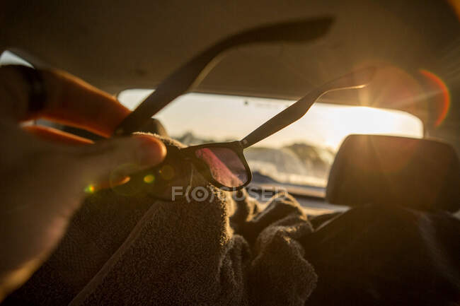 Jovem limpando óculos de sol dentro do carro iluminado pelo sol, close-up — Fotografia de Stock