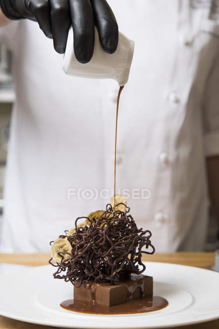 Chef gießt Sahne über Schokoladennestkuchendekoration auf Kuchen — Stockfoto