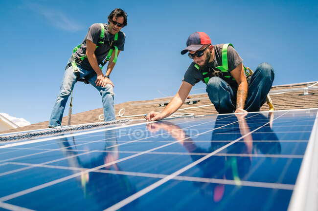 Due operai che installano i pannelli solari sul tetto della casa, vista di angolo basso — Foto stock