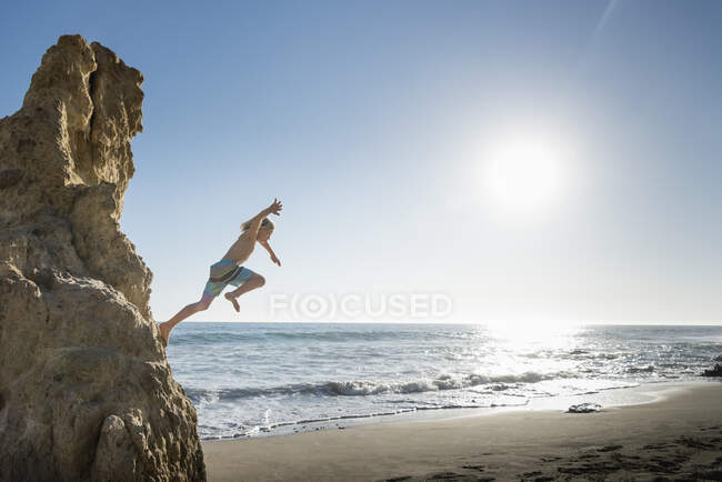 Boy jumping off rock, El Matador Beach, Malibú, Estados Unidos - foto de stock
