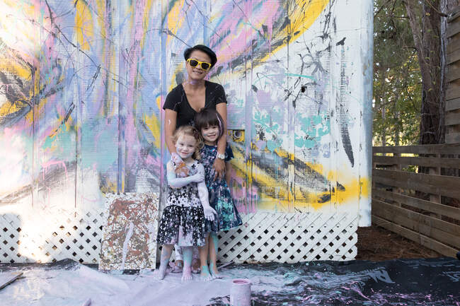 Mother and daughters covered in paint by painted wall — Stock Photo