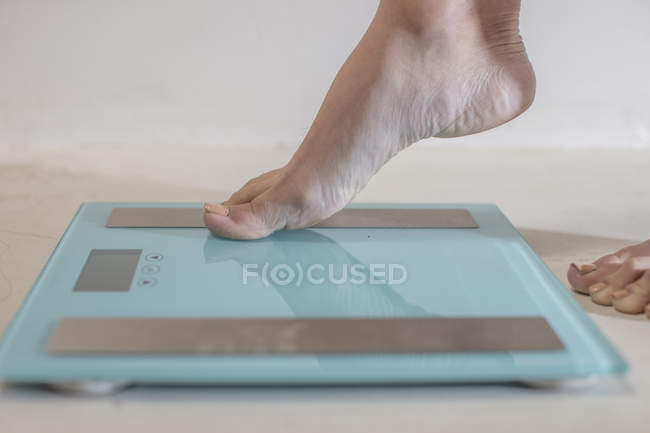 Young woman stepping onto weighing scales — Stock Photo