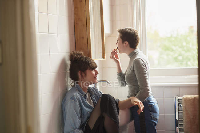 Amigos en baño y mujer aplicando lápiz labial - foto de stock