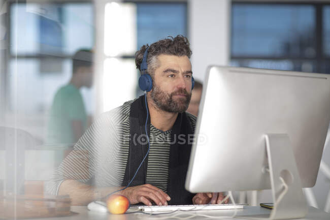 Cape Town, South Africa, man listening to music sitting behind a computer in office — Stock Photo